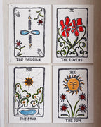 Four illustrated tarot-style cards arranged in a 2x2 grid on a light beige wall. The cards are labeled The Magician, The Lovers, The Star, and The Sun, with black outlines and colorful drawings in red, blue, green, and yellow.