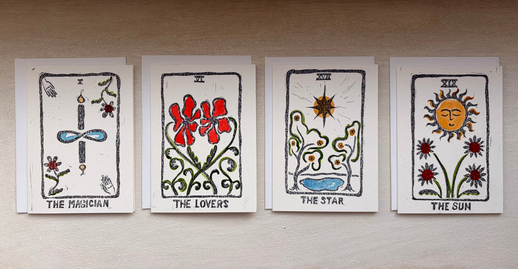 Four illustrated tarot-style cards are stacked vertically on a light beige surface. The cards feature hand-drawn folk art designs including 'THE MAGICIAN, 'THE LOVERS', 'THE STAR', and 'THE SUN'.