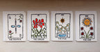 Four illustrated tarot-style cards are stacked vertically on a light beige surface. The cards feature hand-drawn folk art designs including 'THE MAGICIAN, 'THE LOVERS', 'THE STAR', and 'THE SUN'.