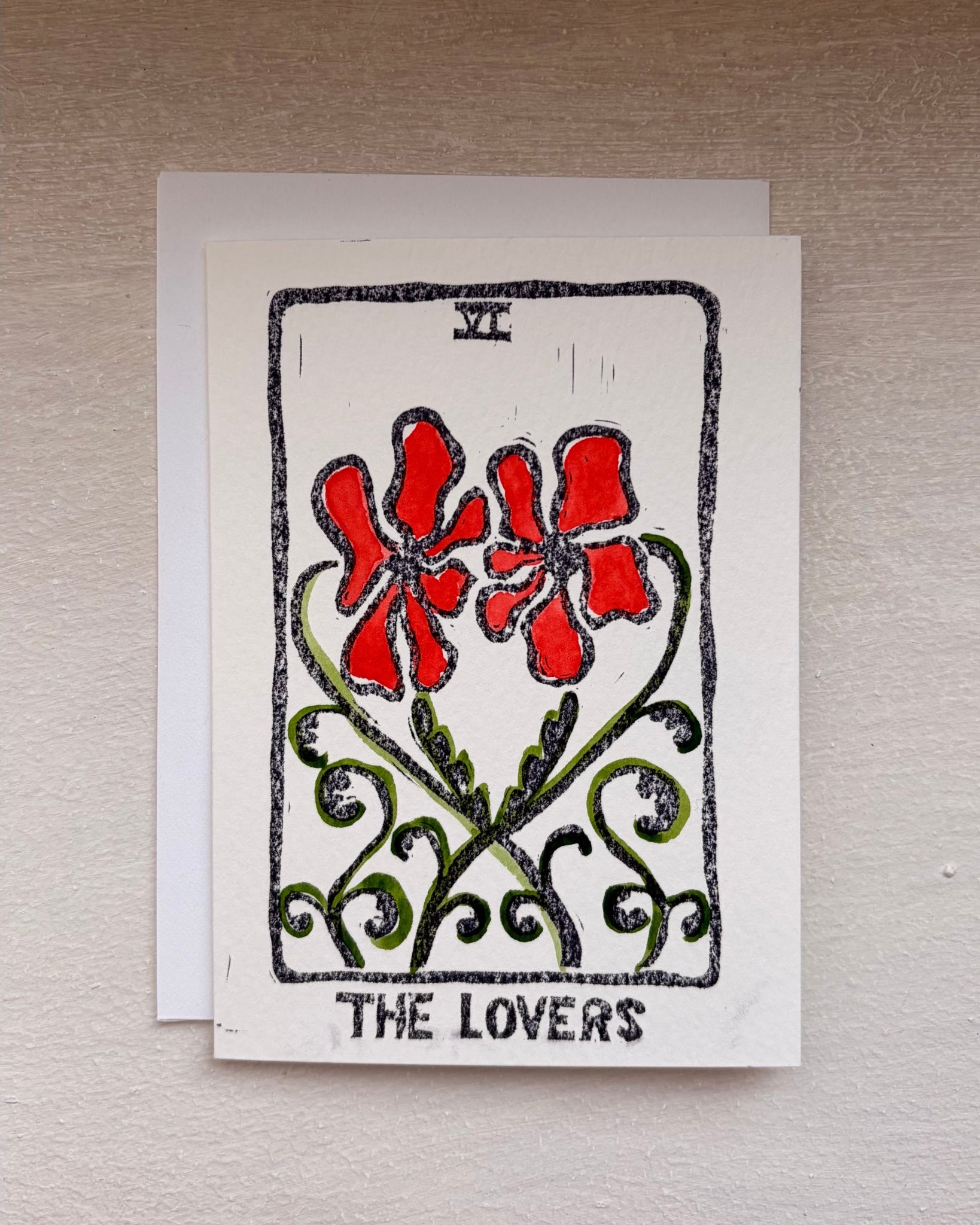 A square art print card featuring a tarot-style illustration labeled 'THE LOVERS' with red flowers, green vines, and black border details, beneath, an envelope.