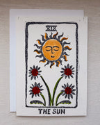 A handmade art print card depicting 'The Sun' tarot card design, featuring a hand-drawn orange sun and red flowers on an off-white textured card with an envelope beneath. 